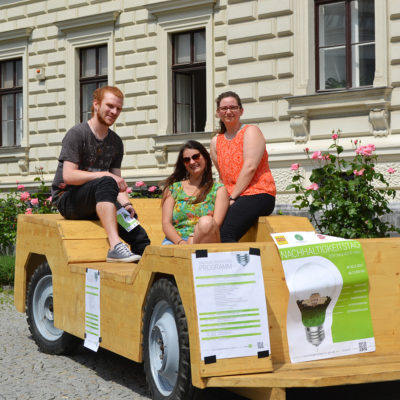 Aircampus Graz Studenten sitzen auf Holzauto